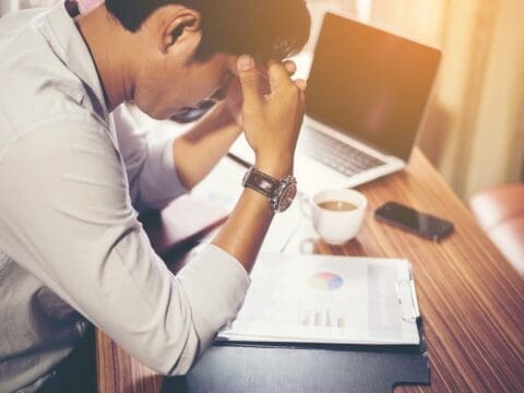 Small Business Cash flow stress, man in front of documents and laptop.
